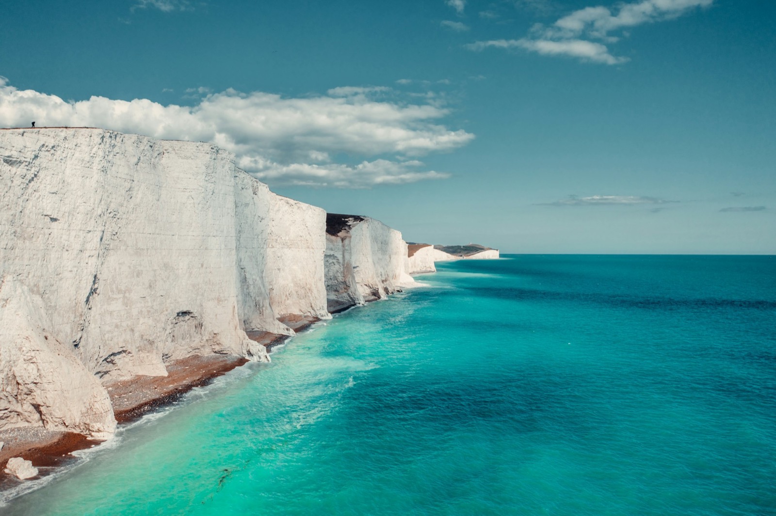 White chalk cliffs above a green-blue sea under a clear sky, on the Sussex coast.